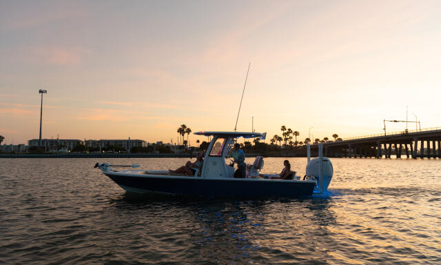 Fishing boat anchored in shallow water at sunset with bridge and palm trees in the distance