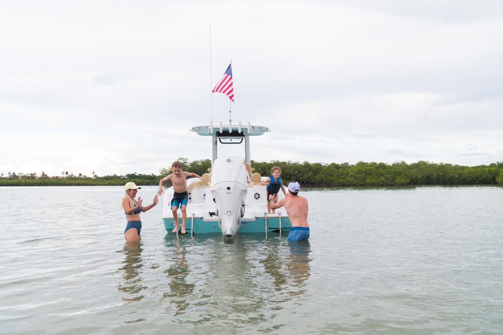 Family swimming and playing in shallow sandbar waters around a center console boat with American flag