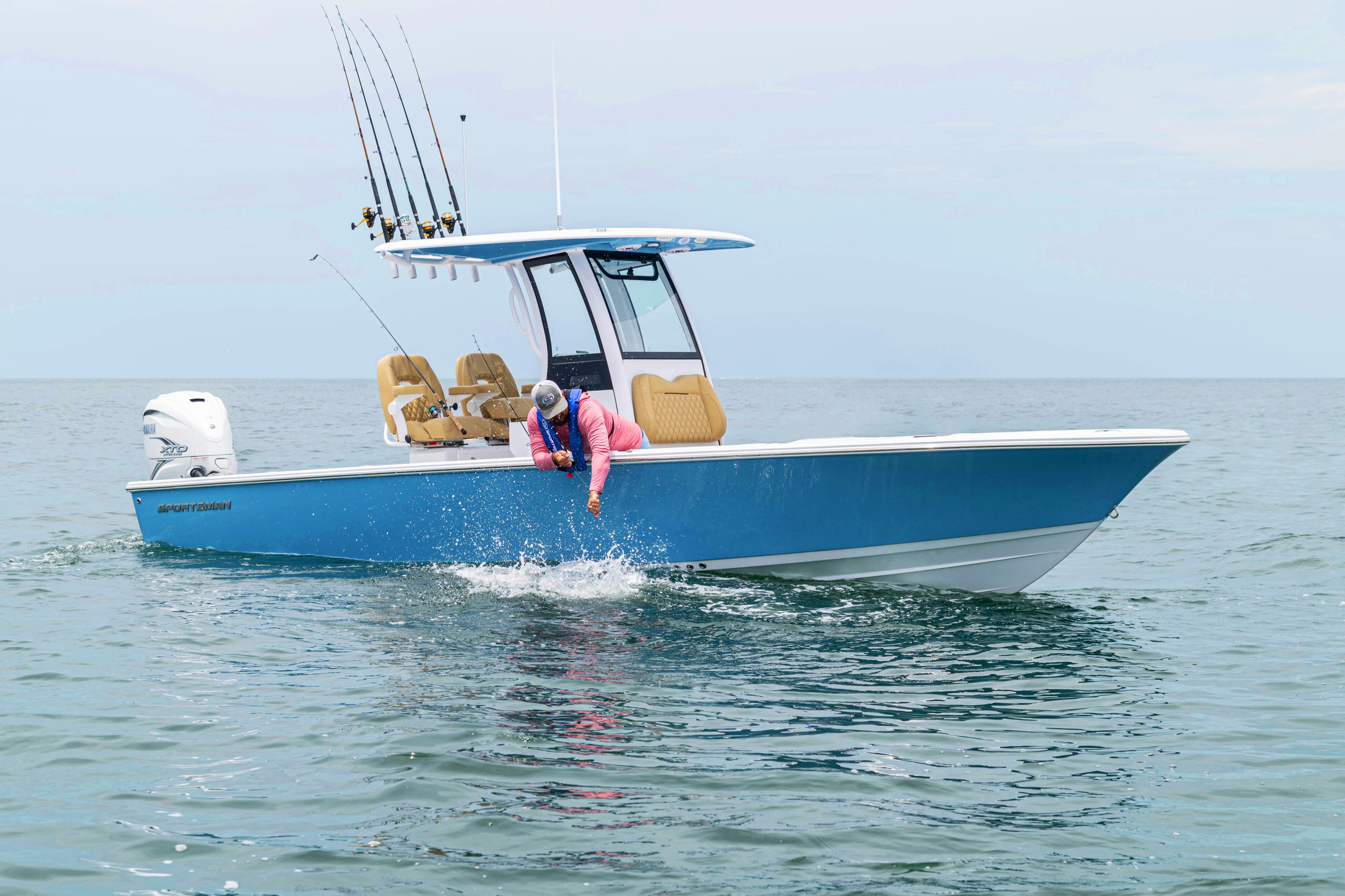 Blue center console fishing boat with rod holders and angler in shallow offshore water
