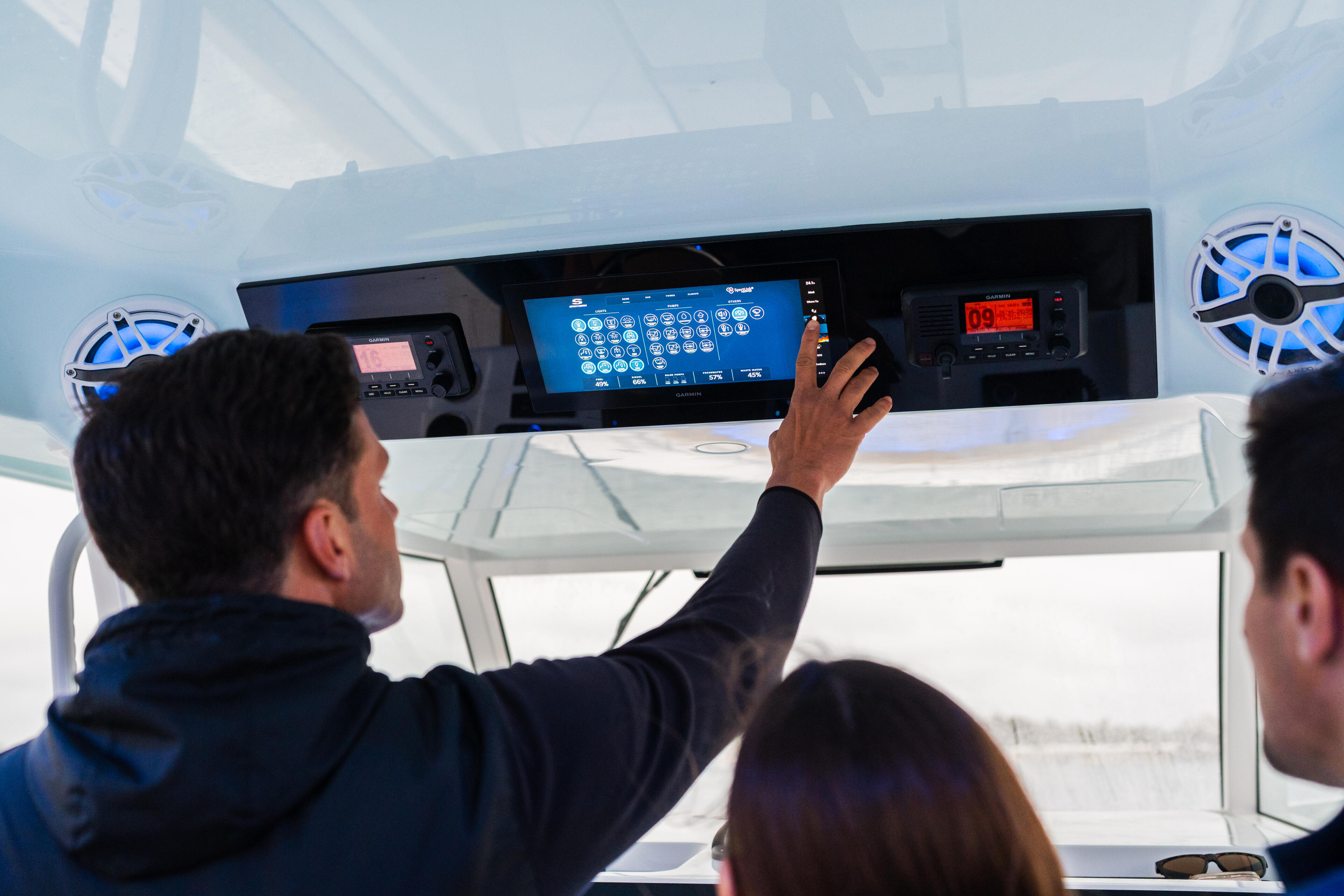 Man operating the helm touchscreen display while two others observe inside the boat's cabin
