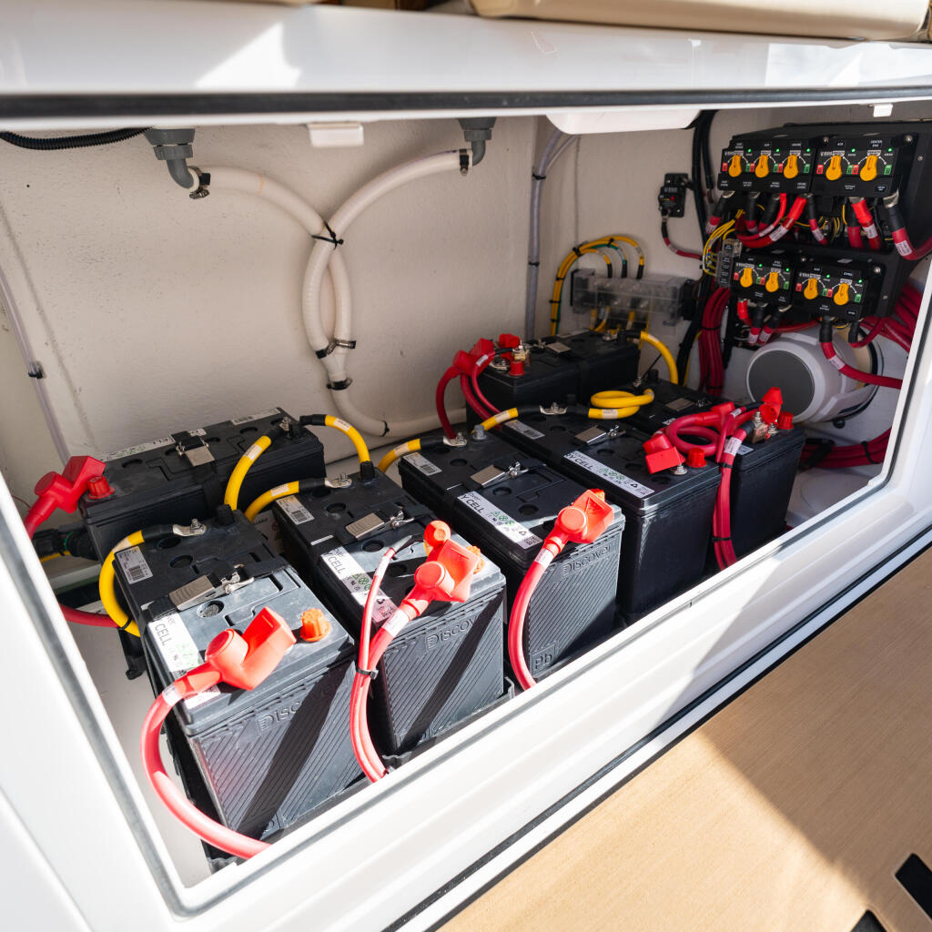 Open engine compartment showing multiple batteries with red and yellow cable connections and electrical panel