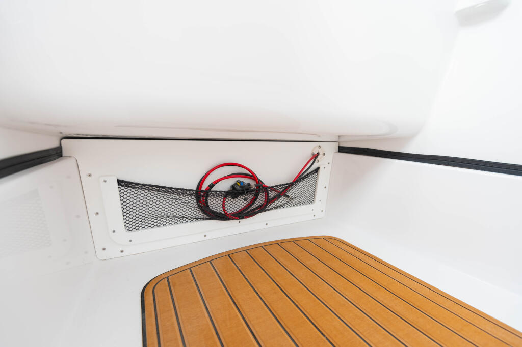 Cabin storage compartment with mesh ventilation panel and red electrical cable coiled inside