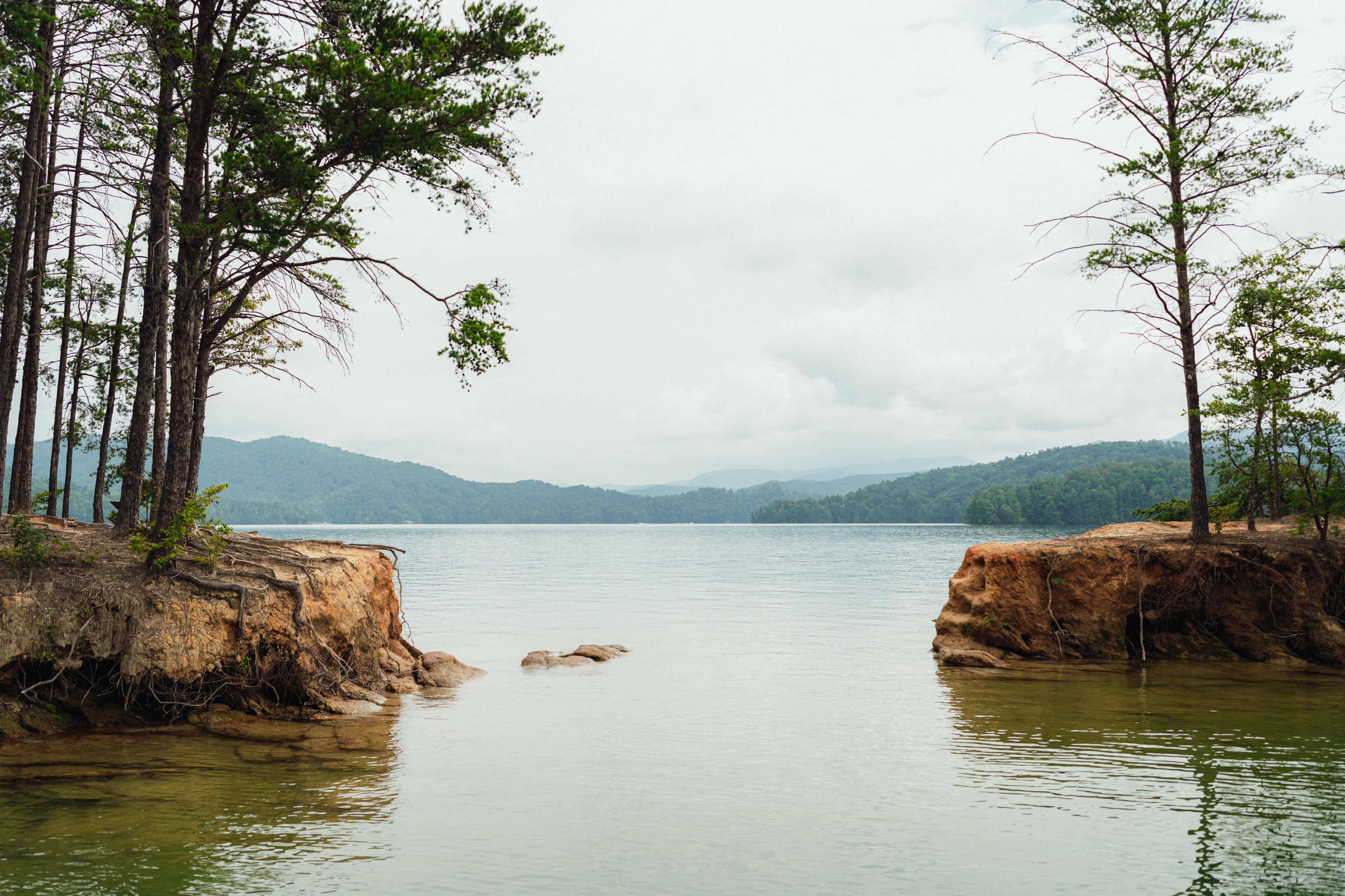 Calm lake surrounded by forested mountains with rocky outcrops framing a peaceful cove