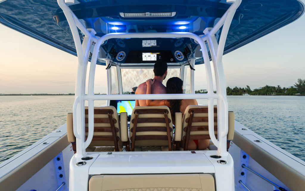 Couple seated under hard-top canopy on center console boat with blue lighting and calm water behind