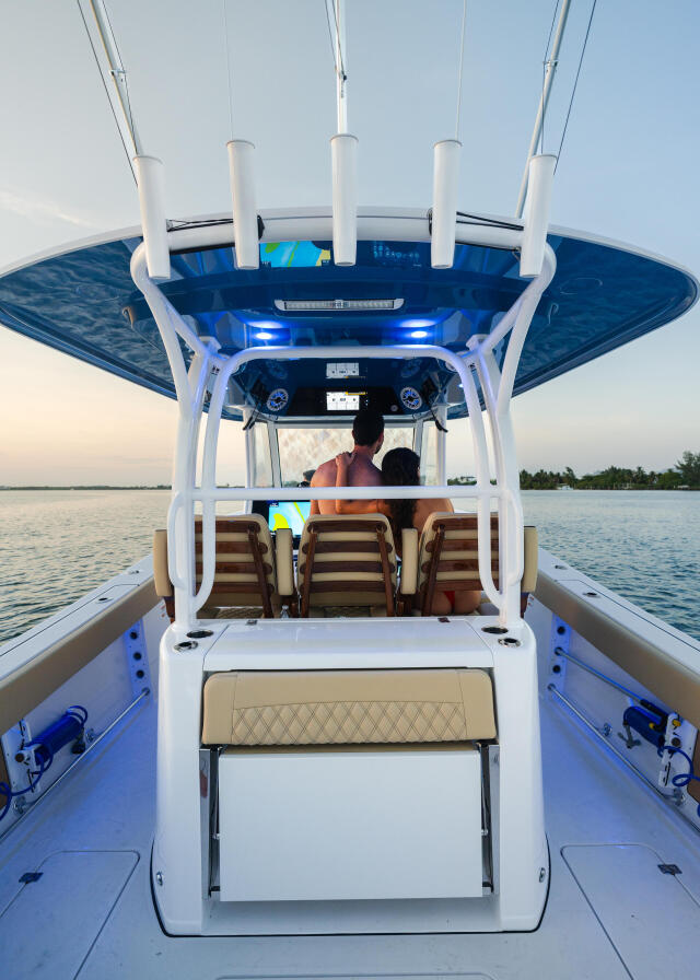 Couple seated under hard-top canopy on center console boat with blue lighting and calm water behind