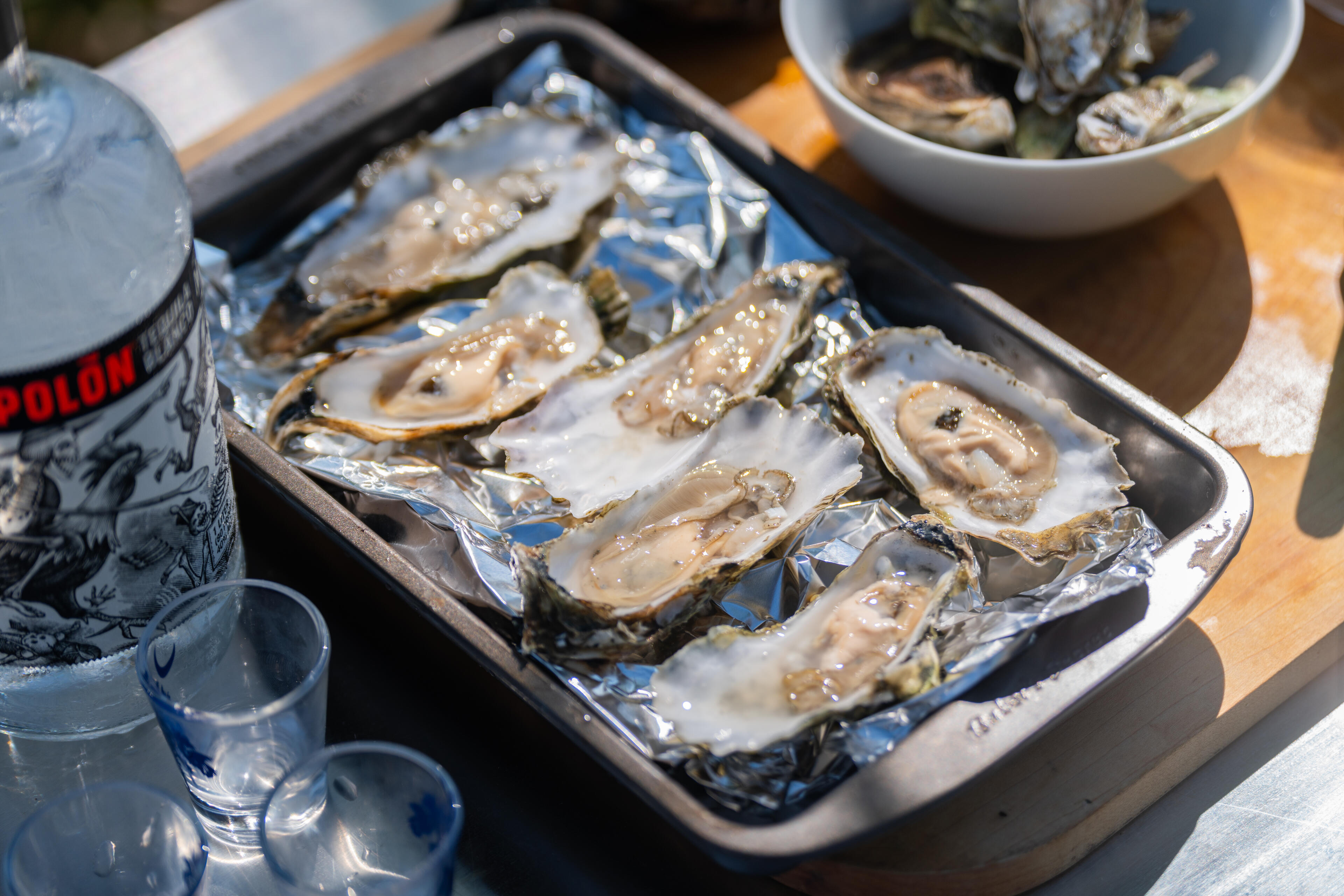 Fresh oysters on ice in a metal tray with cocktails and wine nearby