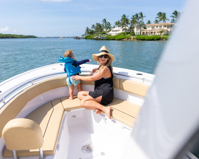 Woman and young child enjoy a sunny day cruising on a center console boat with waterfront homes visible in the background