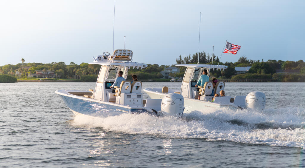 Two white center console boats running through shallow water near a sandbar with families aboard and American flag flying