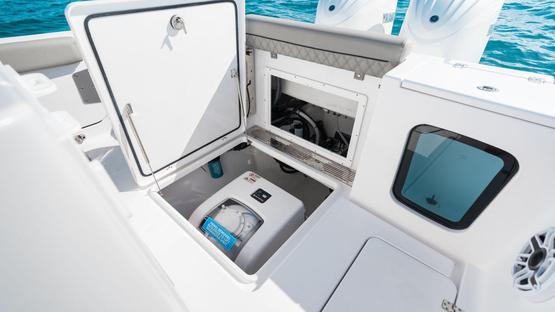 Open storage compartment and engine hatch on a center console boat with twin outboards visible in background
