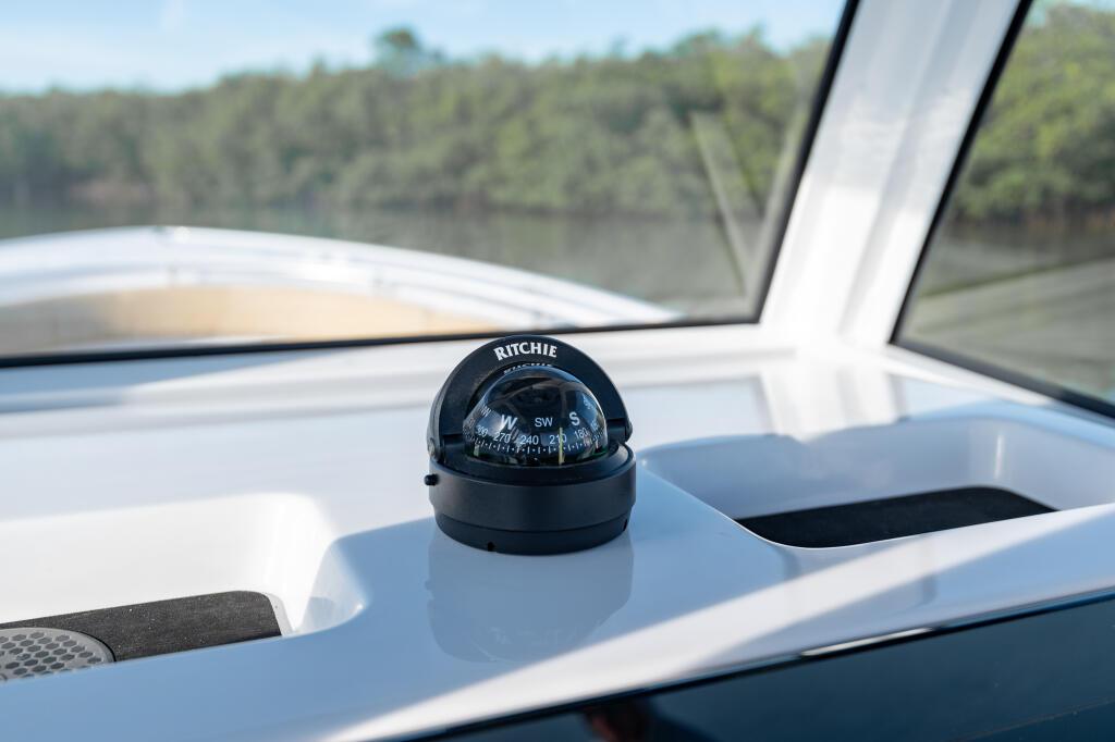 Ritchie compass mounted on the helm of a center console boat with wooded shoreline visible beyond