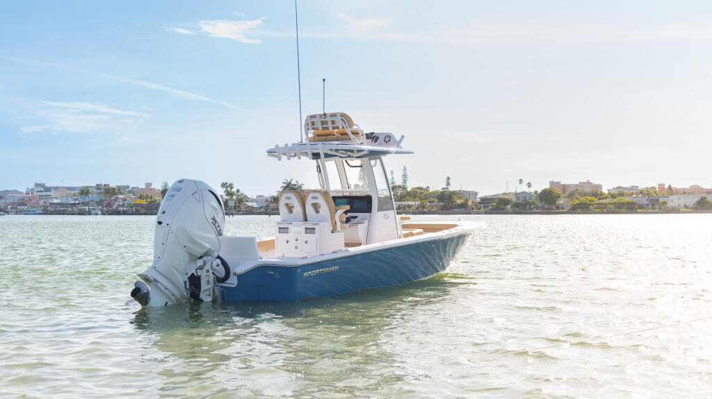 Blue and white sportfishing boat anchored in shallow water near a waterfront neighborhood