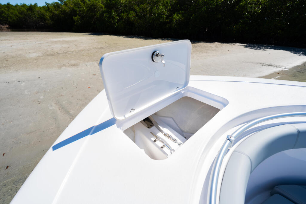 Open boat's white storage compartment and helm seating at a sandy beachside location