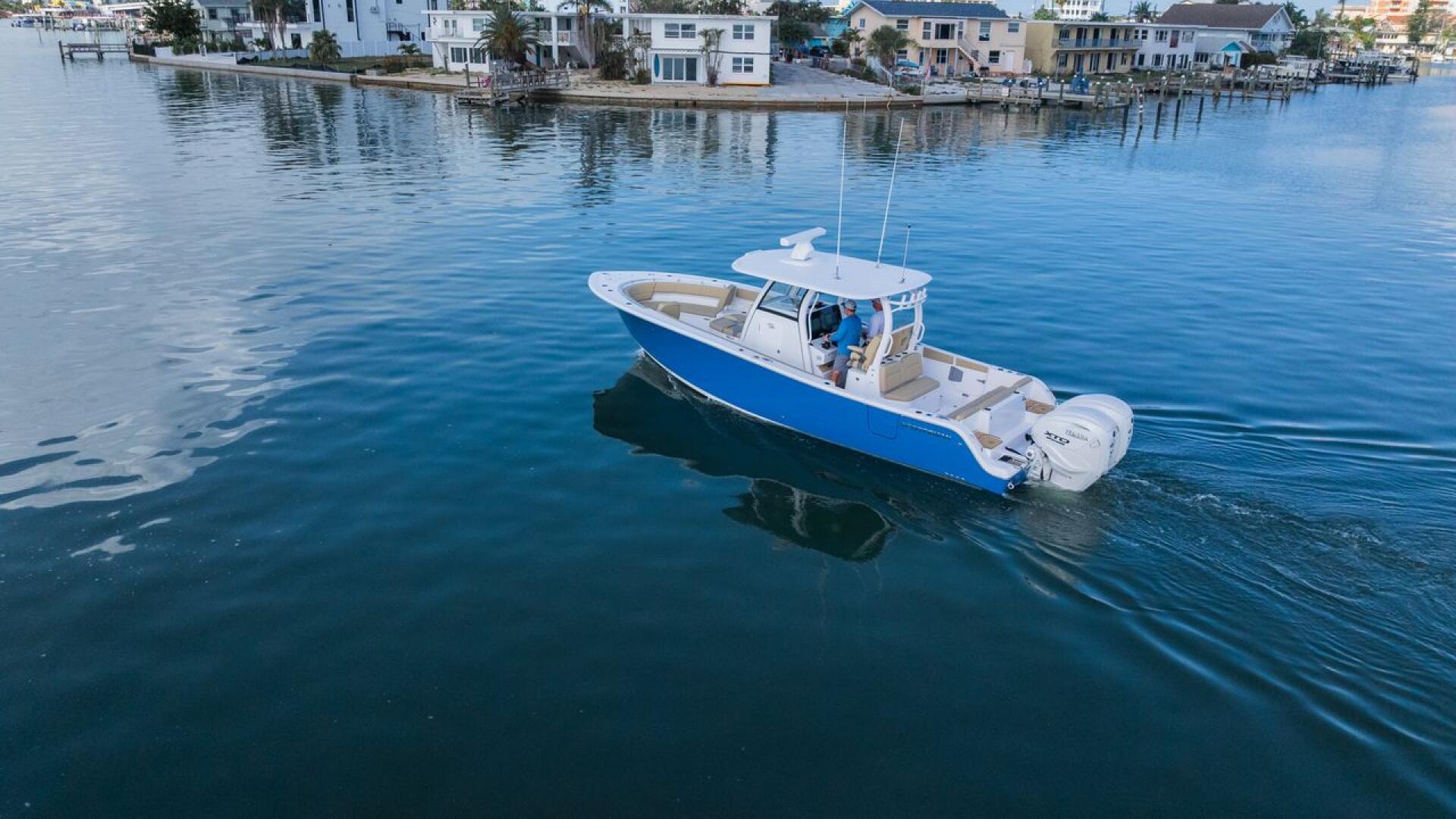 Blue and white fishing boat moored in calm shallow water with waterfront homes and palm trees in background