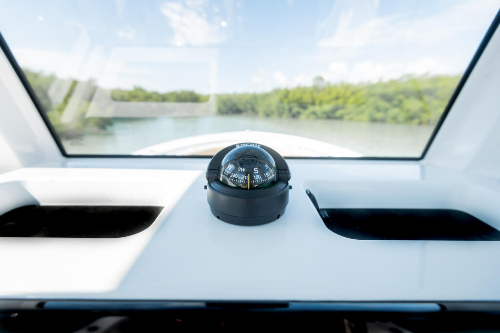 Compass mounted on boat console with river and tree-lined banks visible through windshield