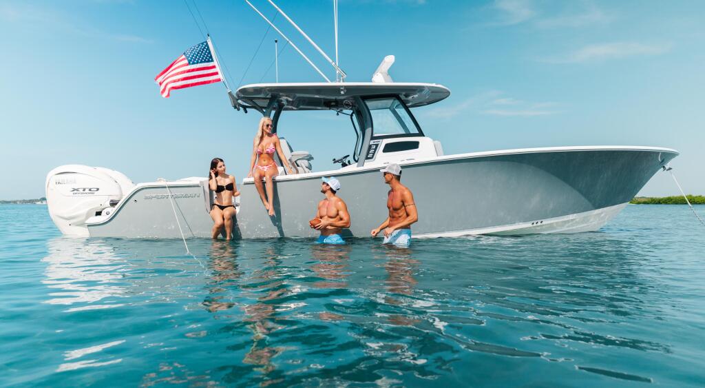 Couples and friends swimming and relaxing in shallow turquoise water beside a center console boat with American flag