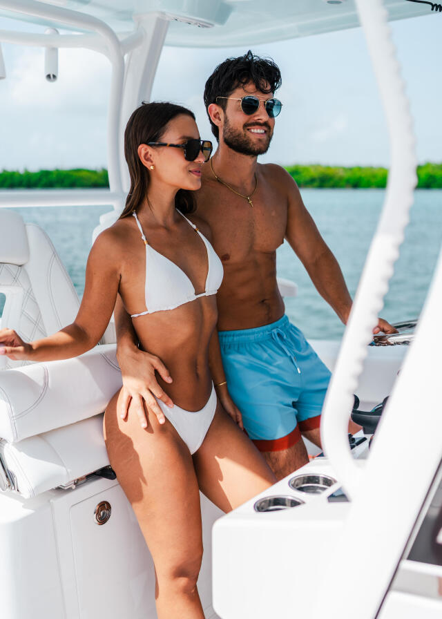 Couple in swimwear enjoying time on a boat helm with water views behind them