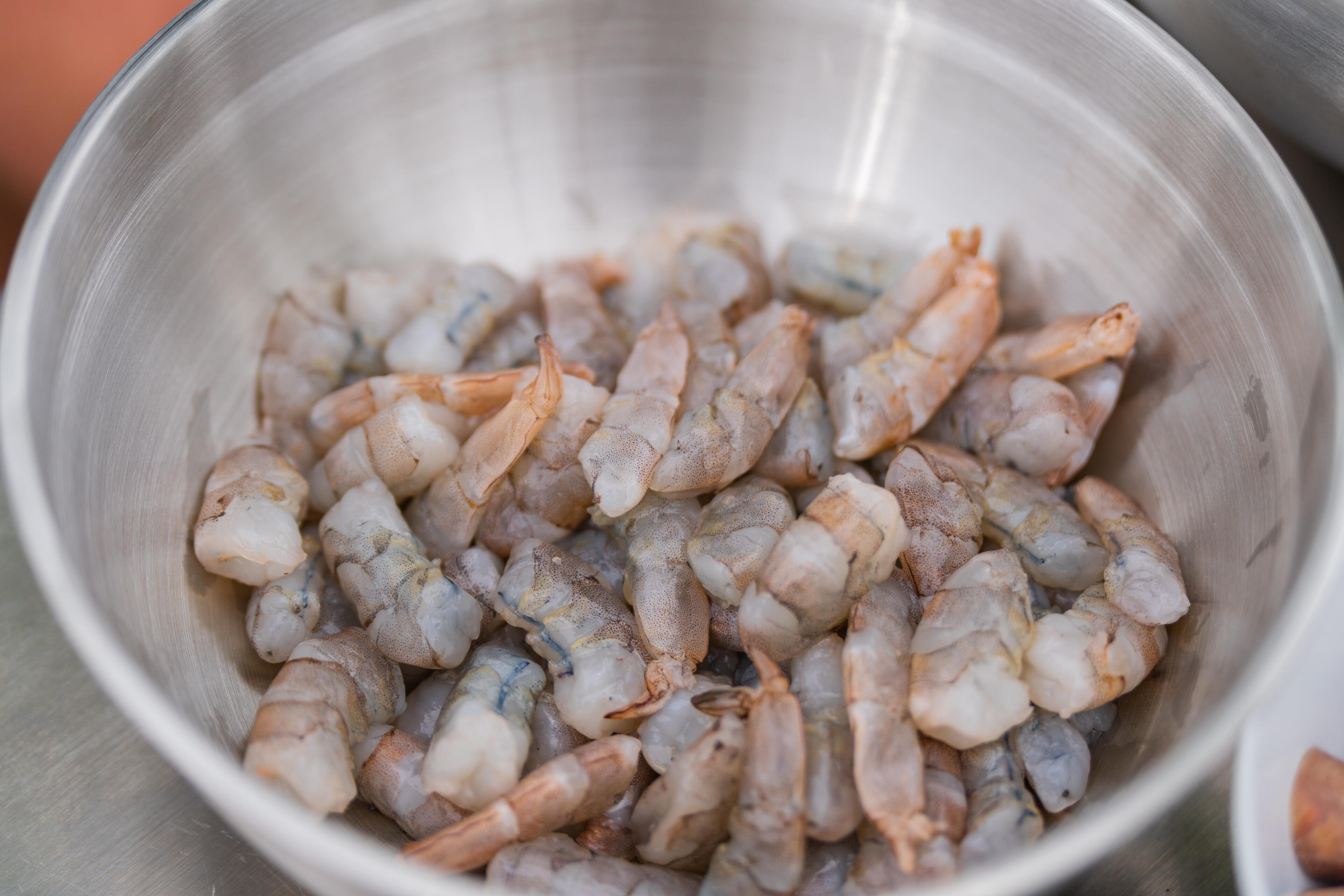 Peeled shrimp in a metal bowl with orange background