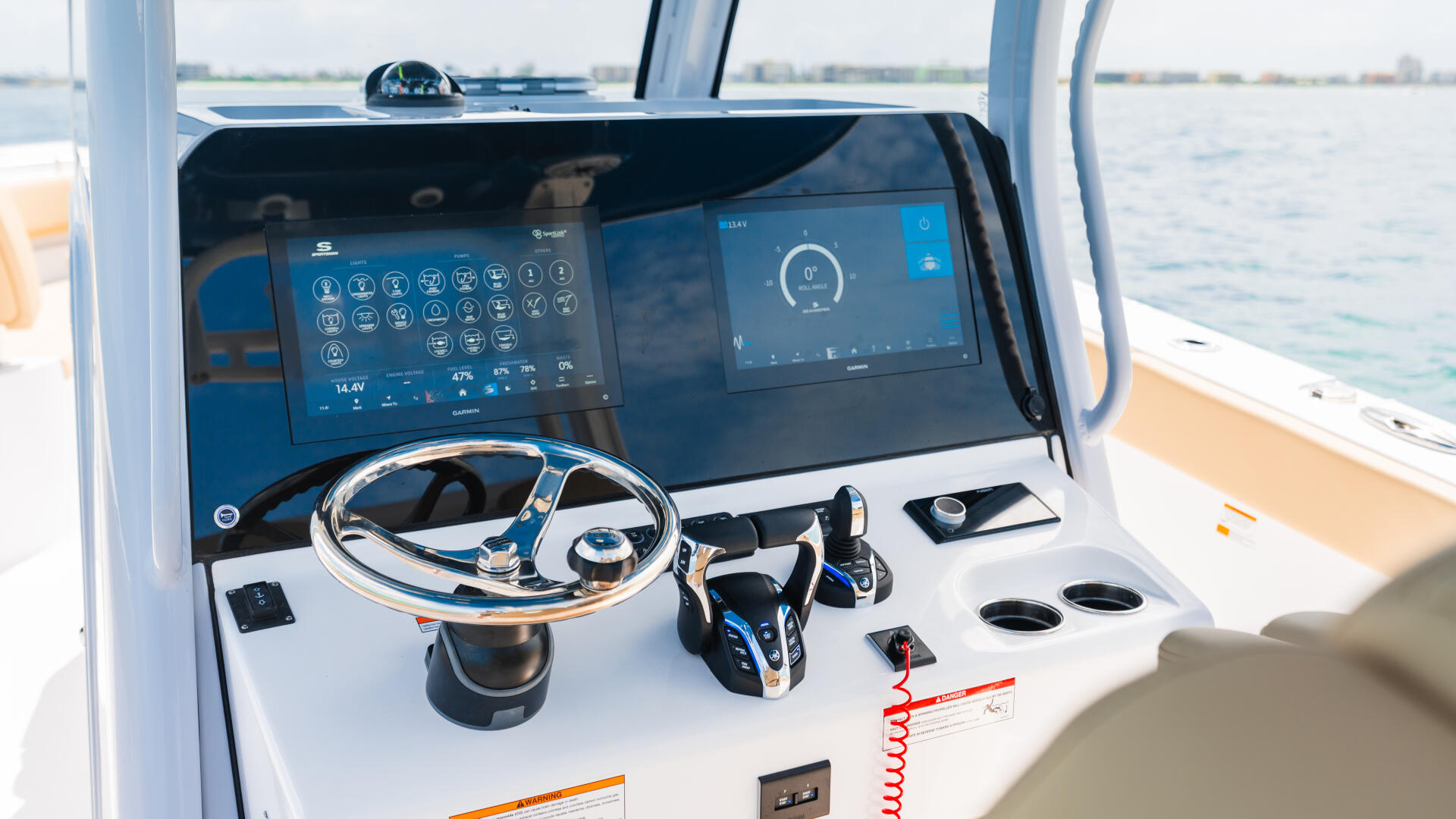 Modern boat helm station with dual touchscreen displays, steering wheel, and control panels overlooking open water