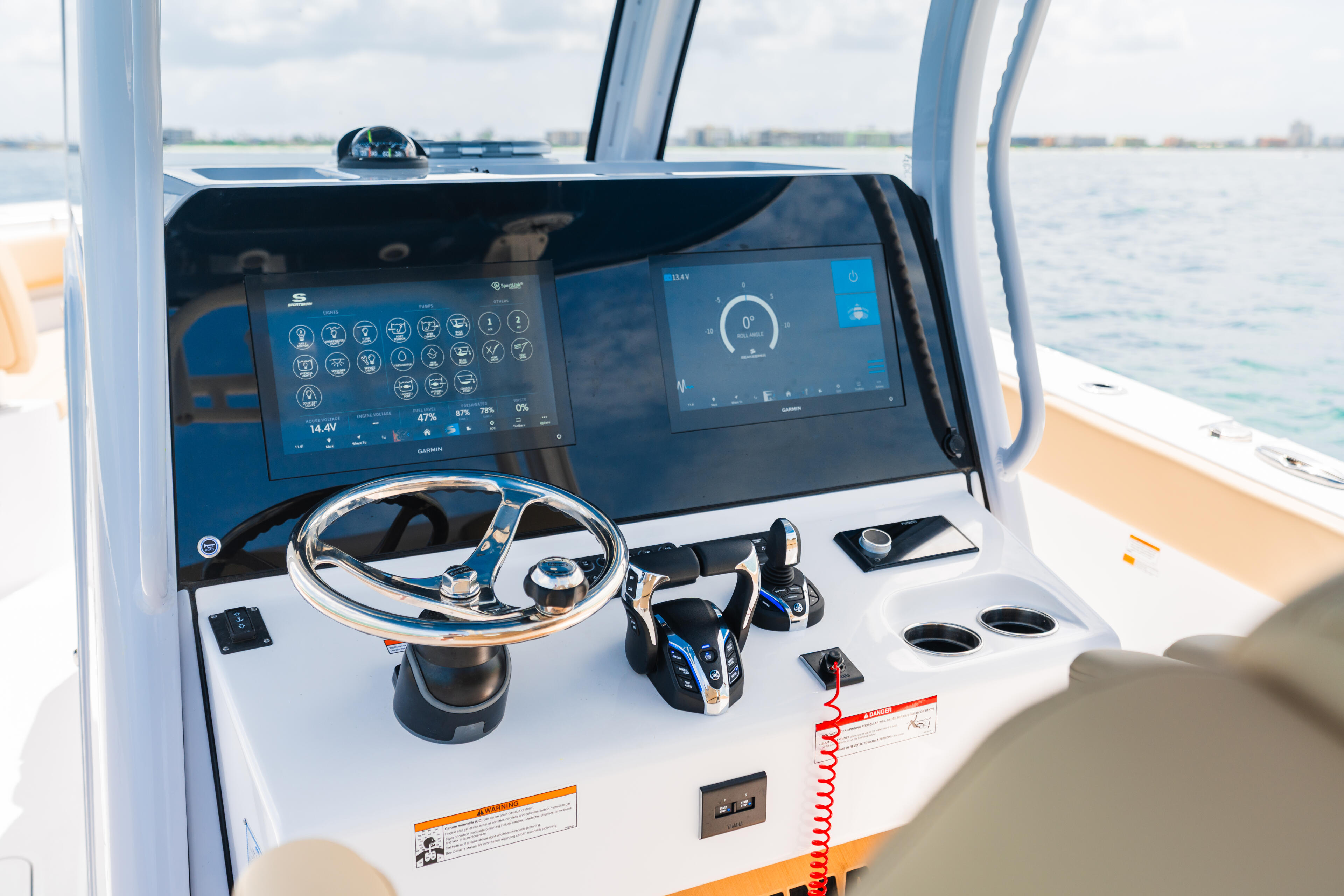 Modern boat helm station with dual touchscreen displays, steering wheel, and control panels overlooking open water