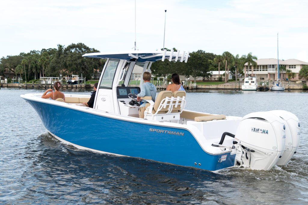 Blue and white center console boat with passengers cruising on calm waterway near residential marina