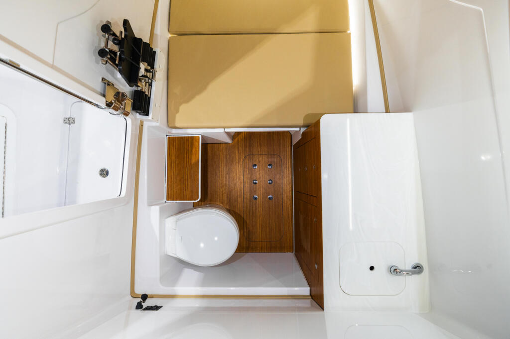 Overhead view of cabin head with white toilet, wood-trimmed walls, and compact storage in white fiberglass berth above