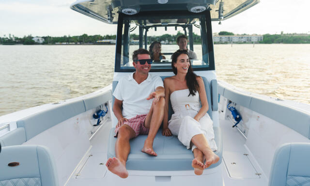 Couple relaxing on the forward seating of a center console boat with friends visible at the helm under the hard-top canopy