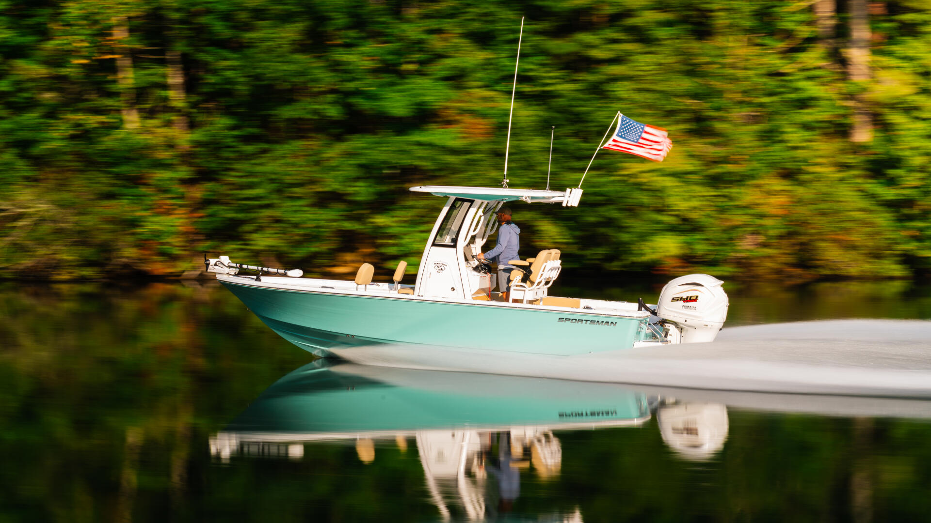Turquoise and white sportsman boat with American flag anchored in calm forest-lined water