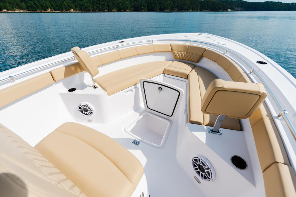 Boat's spacious bow seating area with tan upholstery, storage compartments, and water view