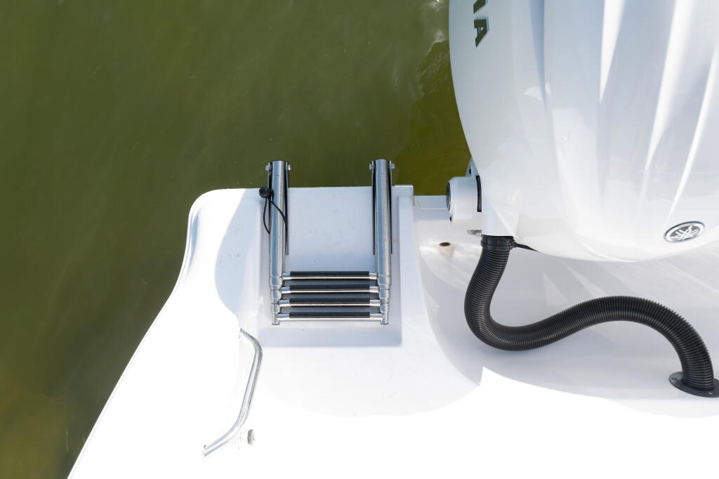 Overhead view of boat's swim platform with stainless steel boarding ladder and drainage hose in calm shallow water