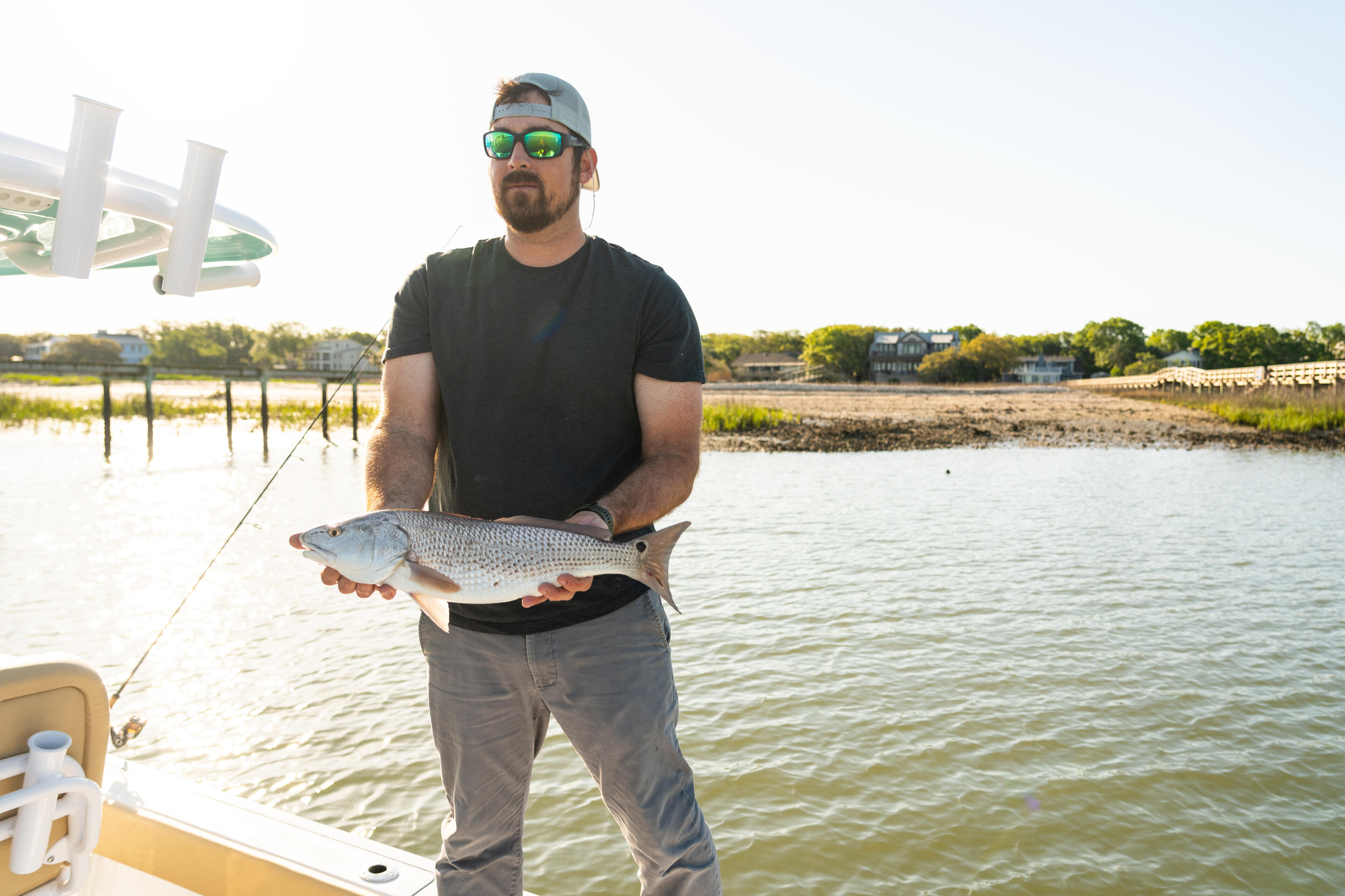 Angler holds a caught redfish while standing on a boat in shallow coastal waters