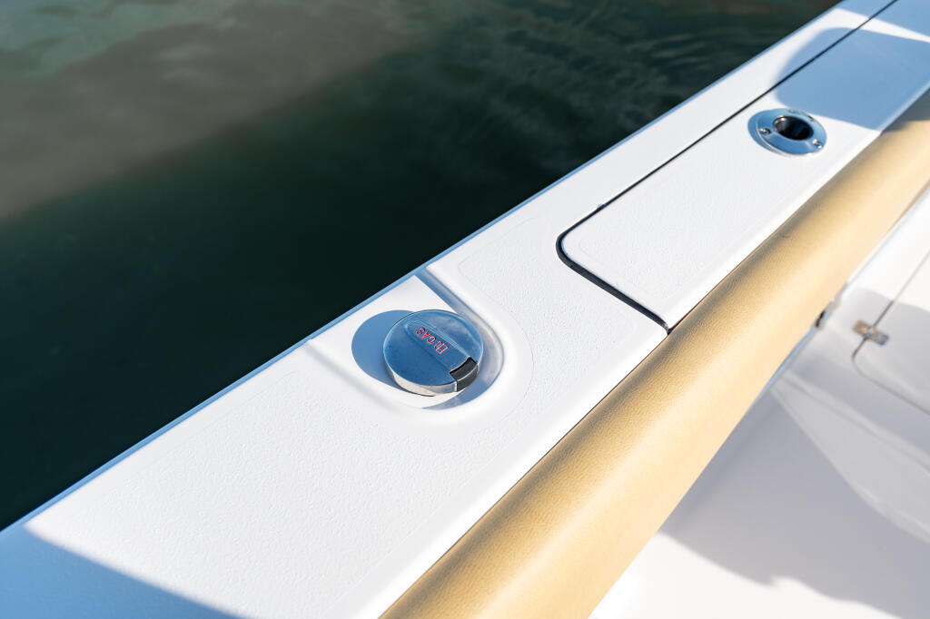 Close-up of boat gunwale showing dual fuel fill caps and cleats with water alongside