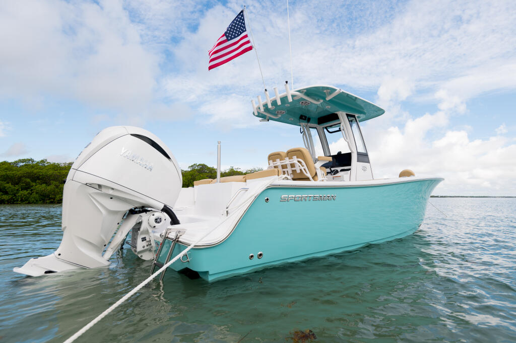 Turquoise and white center console boat anchored in shallow water with hard-top canopy and American flag