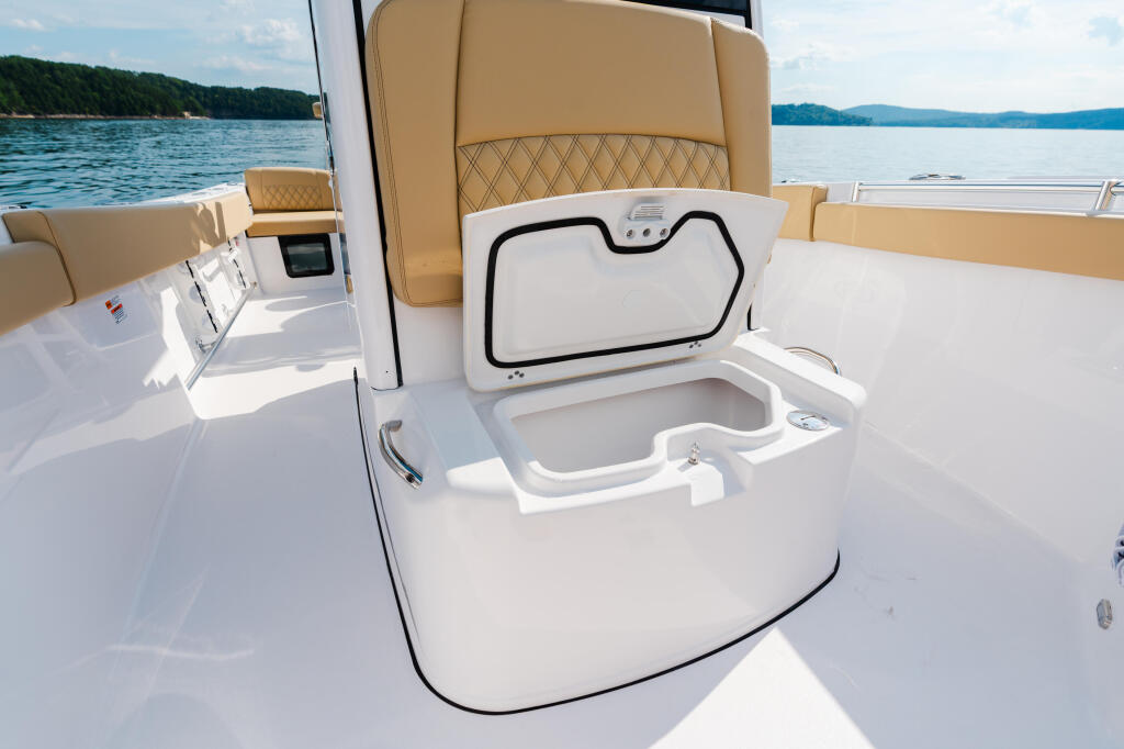 Open livewell and storage compartments on boat deck with tan seating and calm lake view
