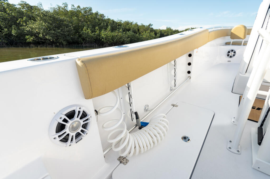 Starboard gunwale with tan bolster cushioning, coiled white hose, speaker, and mangrove shoreline in background
