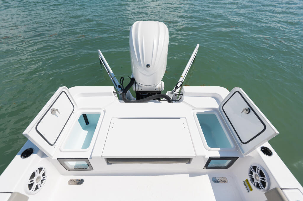Overhead view of boat helm station with white hardtop, dual consoles, and twin outboard engines on calm turquoise water