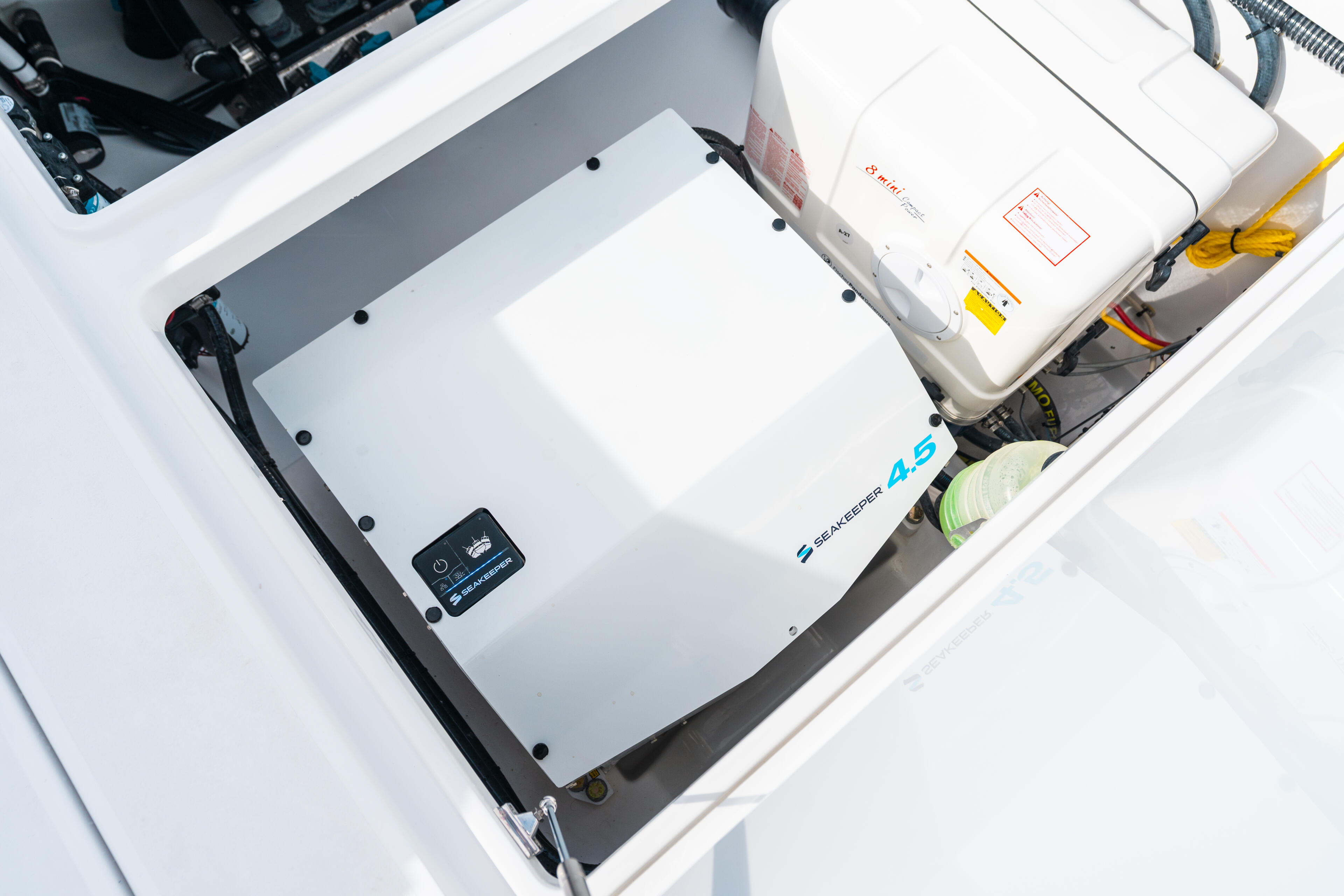 Overhead view of boat's open storage locker with sealed container, electronics panel, fishing gear, and yellow rope