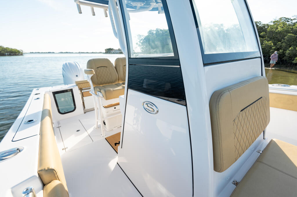 Helm station and tan upholstered seating inside center console boat with large windows and water view