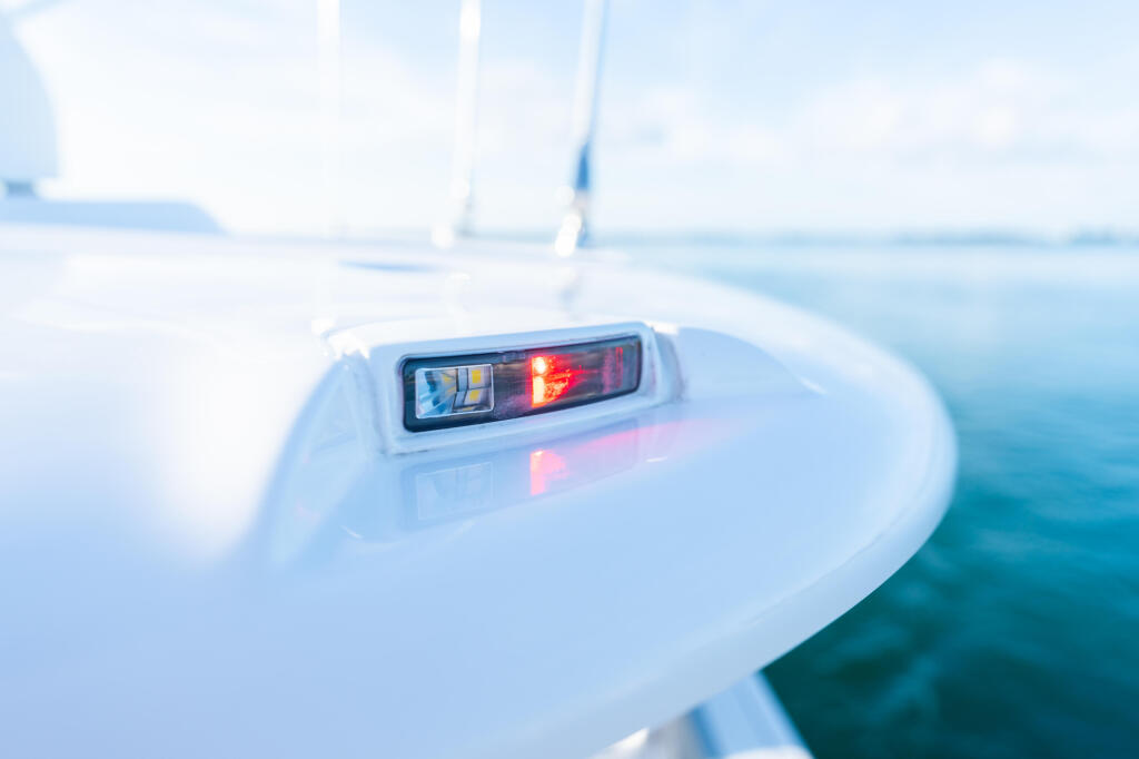 Red and white navigation light mounted on the white hardtop of a boat on calm blue water