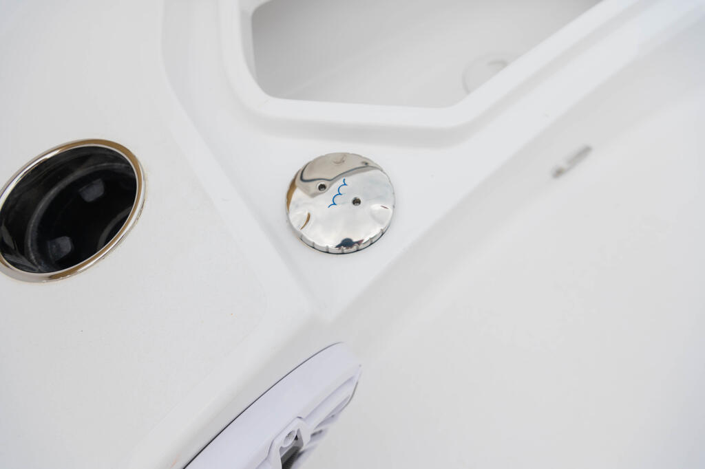 Close-up of boat deck hardware including a circular access port and rinse fitting on white fiberglass
