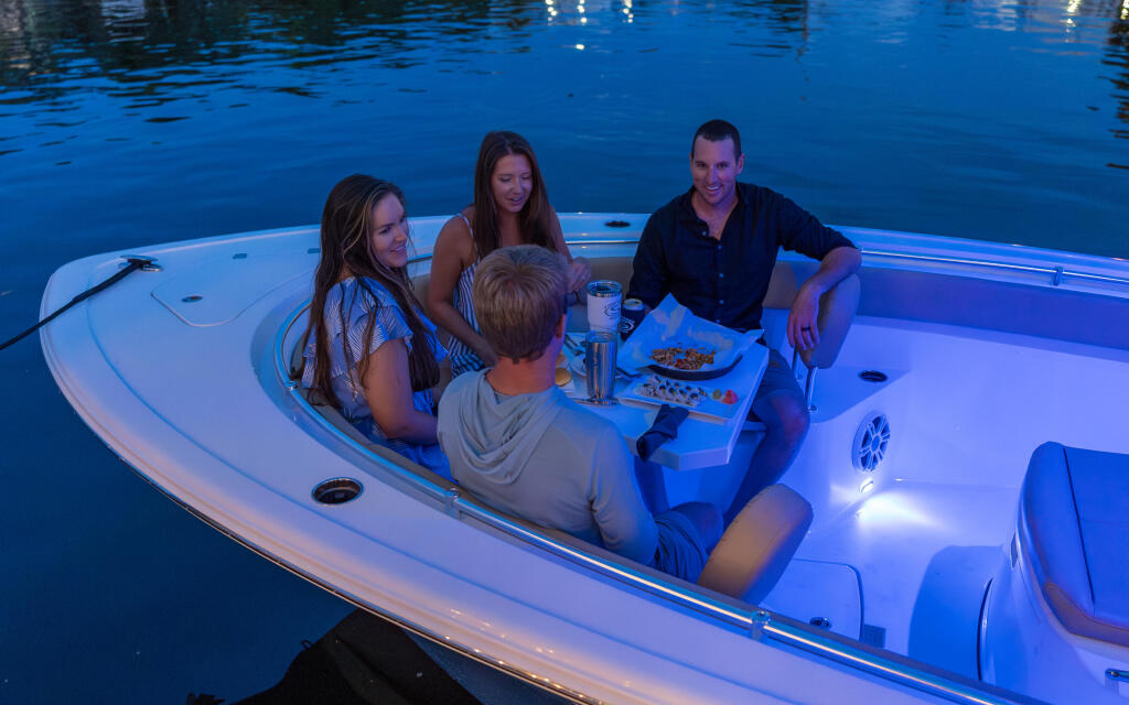 Family of four enjoying an evening meal on a white center console boat with blue LED lighting