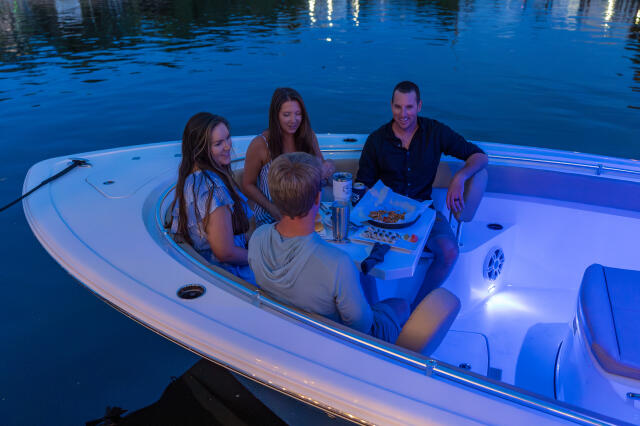 Family of four enjoying an evening meal on a white center console boat with blue LED lighting