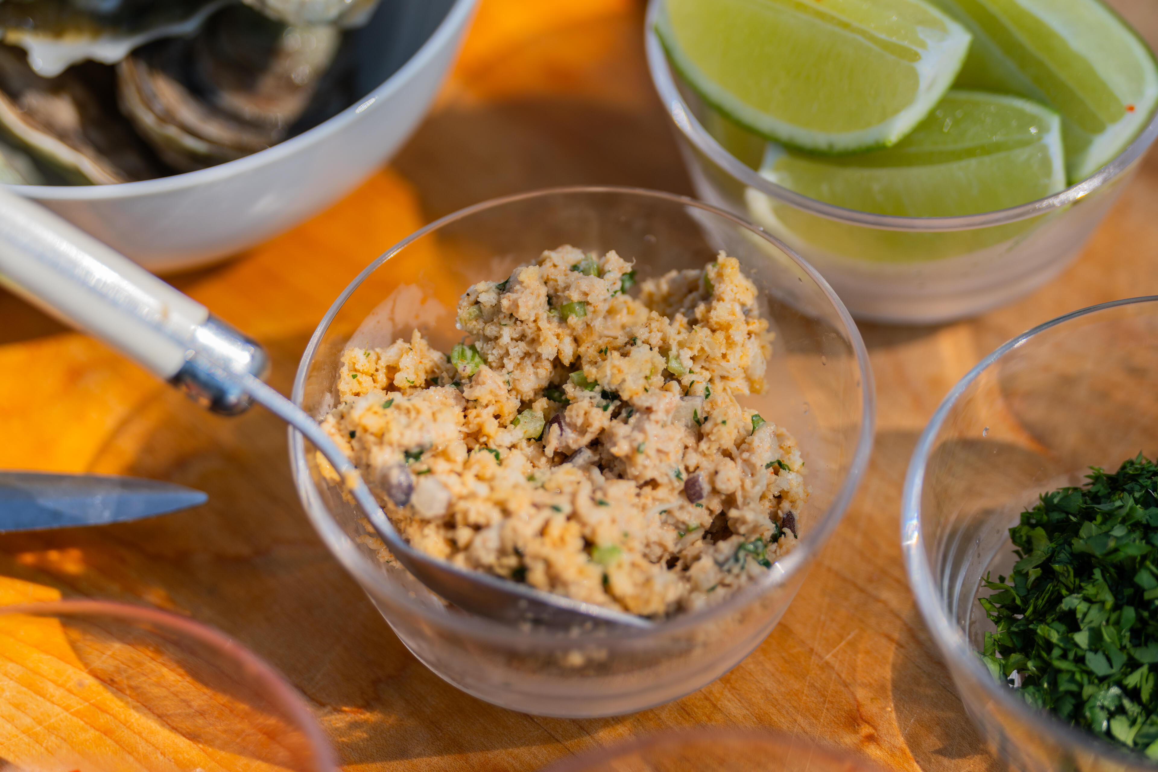 Prepared oyster mixture in a glass bowl with lime wedges and fresh herbs nearby on a wooden surface