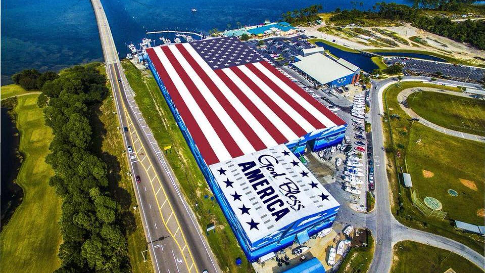 Aerial view of a massive American flag display at a waterfront facility with marina, parking, and coastal infrastructure