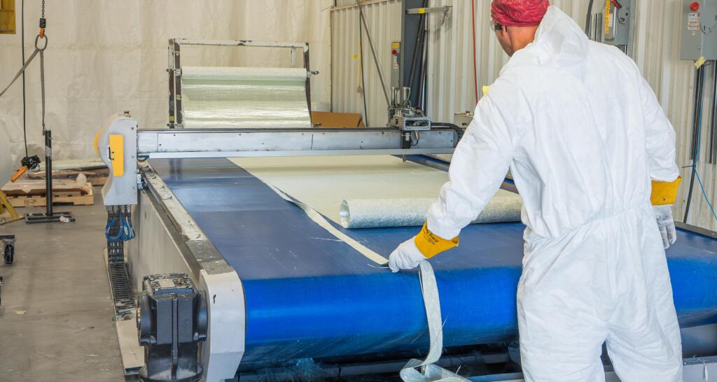 Worker in protective gear applying blue laminate material to a boat hull during advanced fabrication process