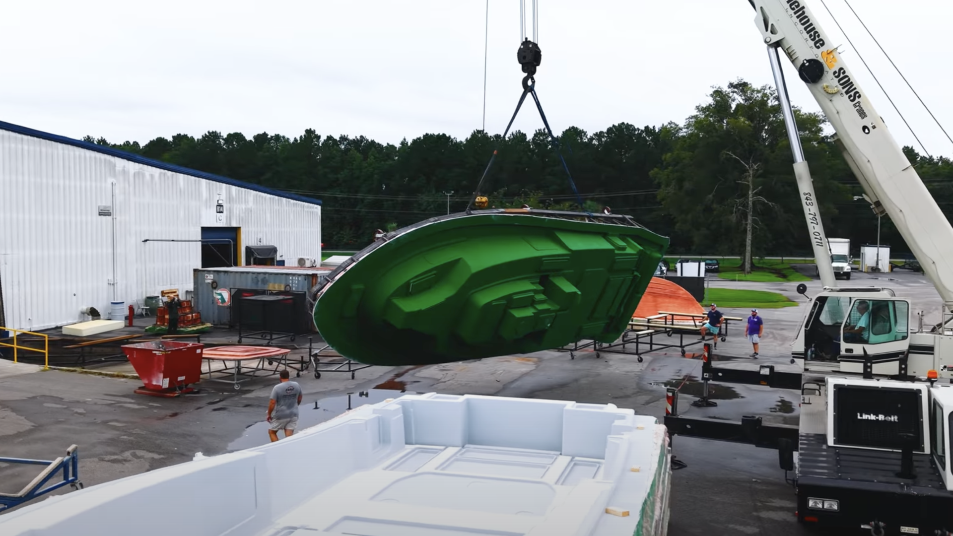 Boat hull being lifted by crane at marina facility with workers and equipment surrounding the work area
