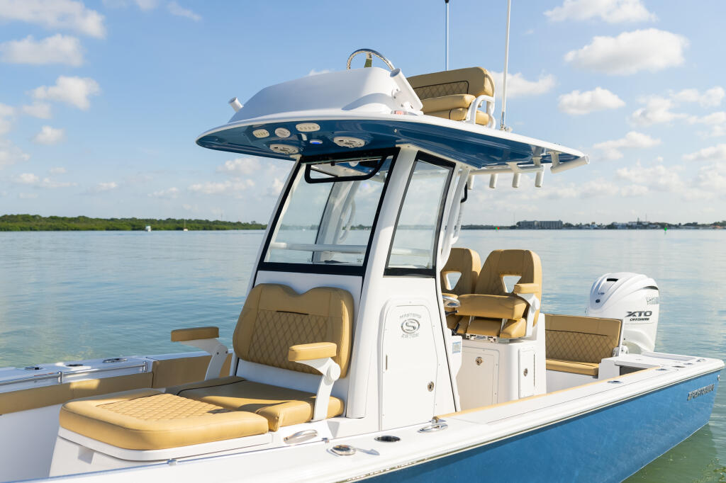 Blue and white center console boat with hard-top, tan seating, and outboard motor on calm water