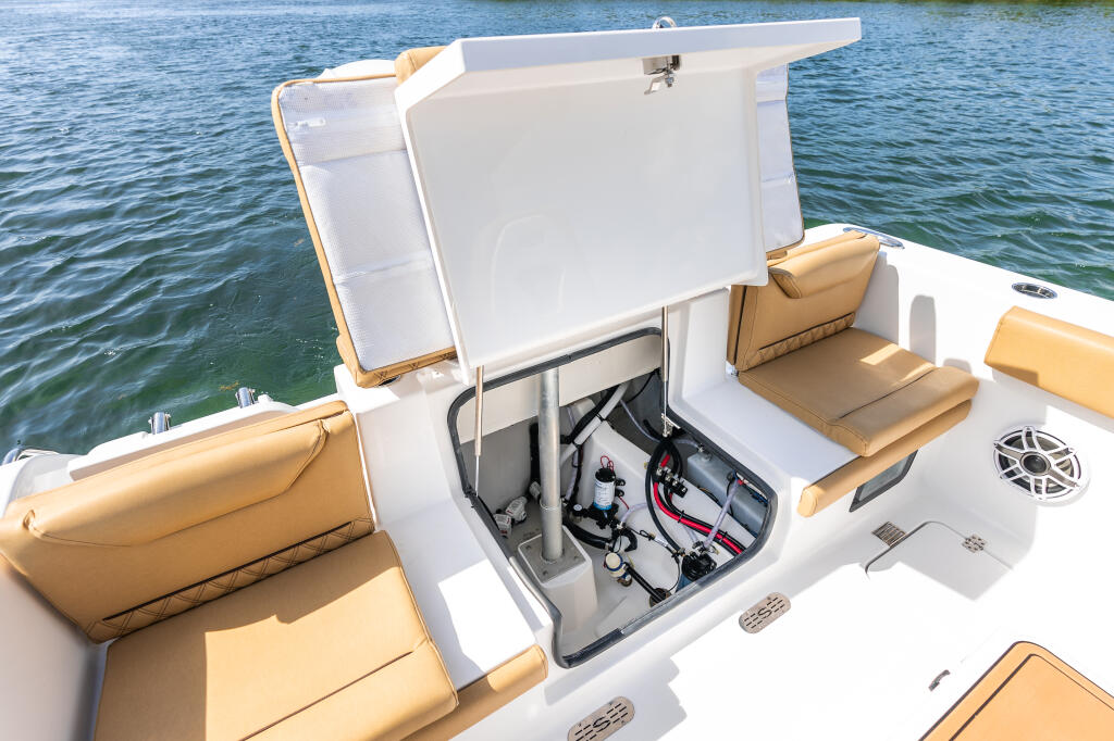 Open engine hatch revealing battery, wiring, and mechanical components on a center console boat with tan seating