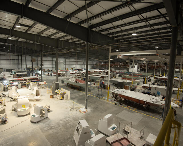 Expansive boat manufacturing facility with multiple vessels in various stages of production under industrial steel roof structure