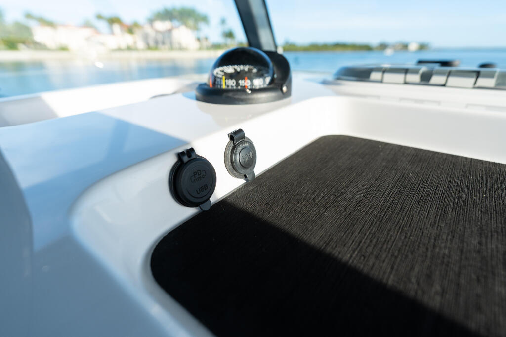 Close-up of boat helm electronics including compass and USB ports with coastal waterfront in background