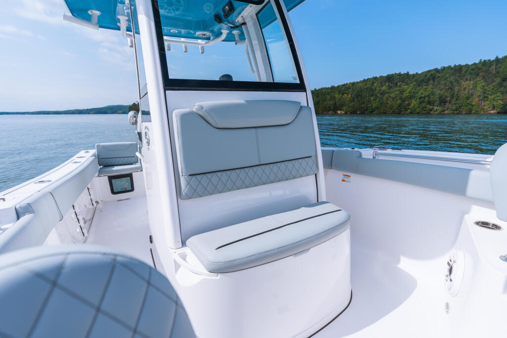 White center console boat with gray seating and windshield on calm lake surrounded by forested shoreline